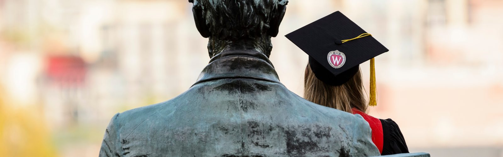 A soon-to-be graduate sits in the lap of the Abraham Lincoln statue on Bascom Hill at the University of Wisconsin-Madison and poses for a photo wearing her graduation mortarboard during a sunny afternoon on May 10, 2018. Colder weather and rain is in the forecast for much of UW-Madison's spring commencement weekend. (Photo by Jeff Miller / UW-Madison)