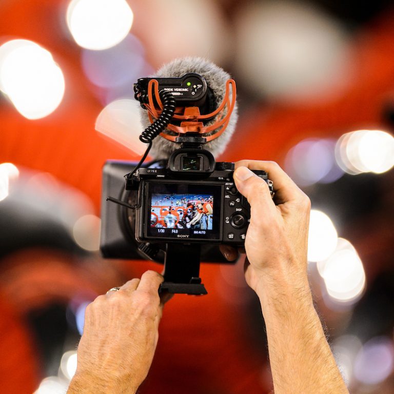 A person's hands holding up a camera with the UW Marching Band on the preview screen.