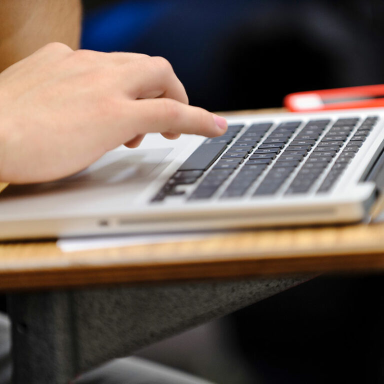 A student takes notes on a laptop computer.