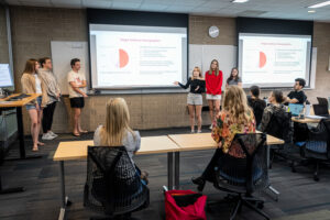 A group of students present data to a classroom of fellow students and professors.