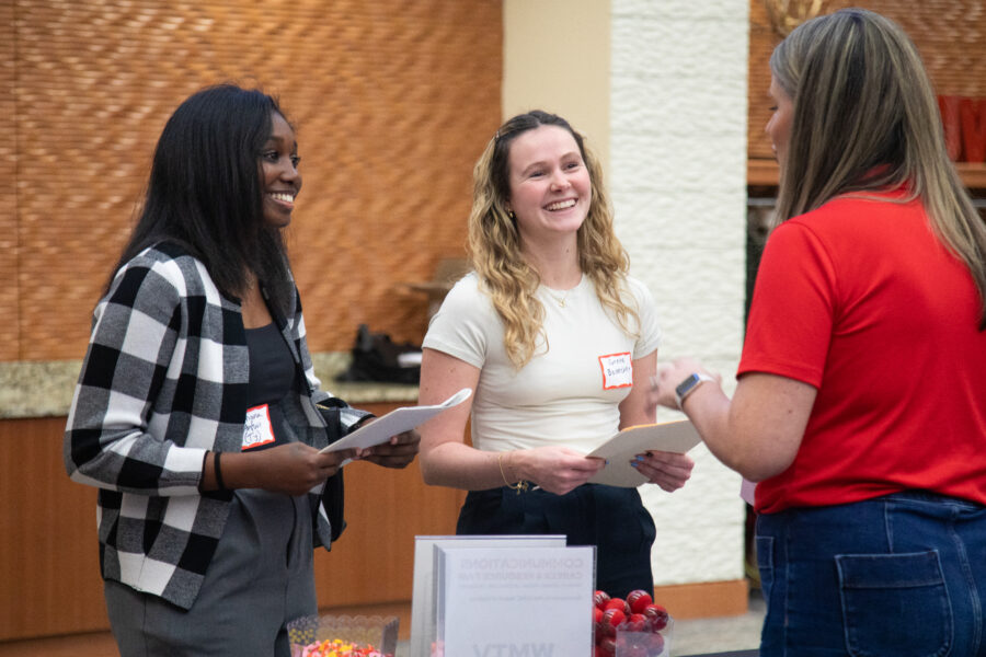 Two female students talk to an employer at a career fair.