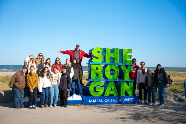 Students in Professor Doug McLeod's J445 Creative Campaign Messages class pose together in front of a Sheboygan sign while on a field trip to Sheboygan.
