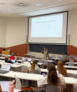 Teaching faculty Adam Schrager stands at the front of a lecture hall teaching course material.