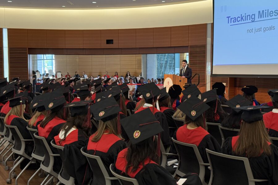 An auditorium filled with graduates watching the keynote speaker at their graduation celebration.
