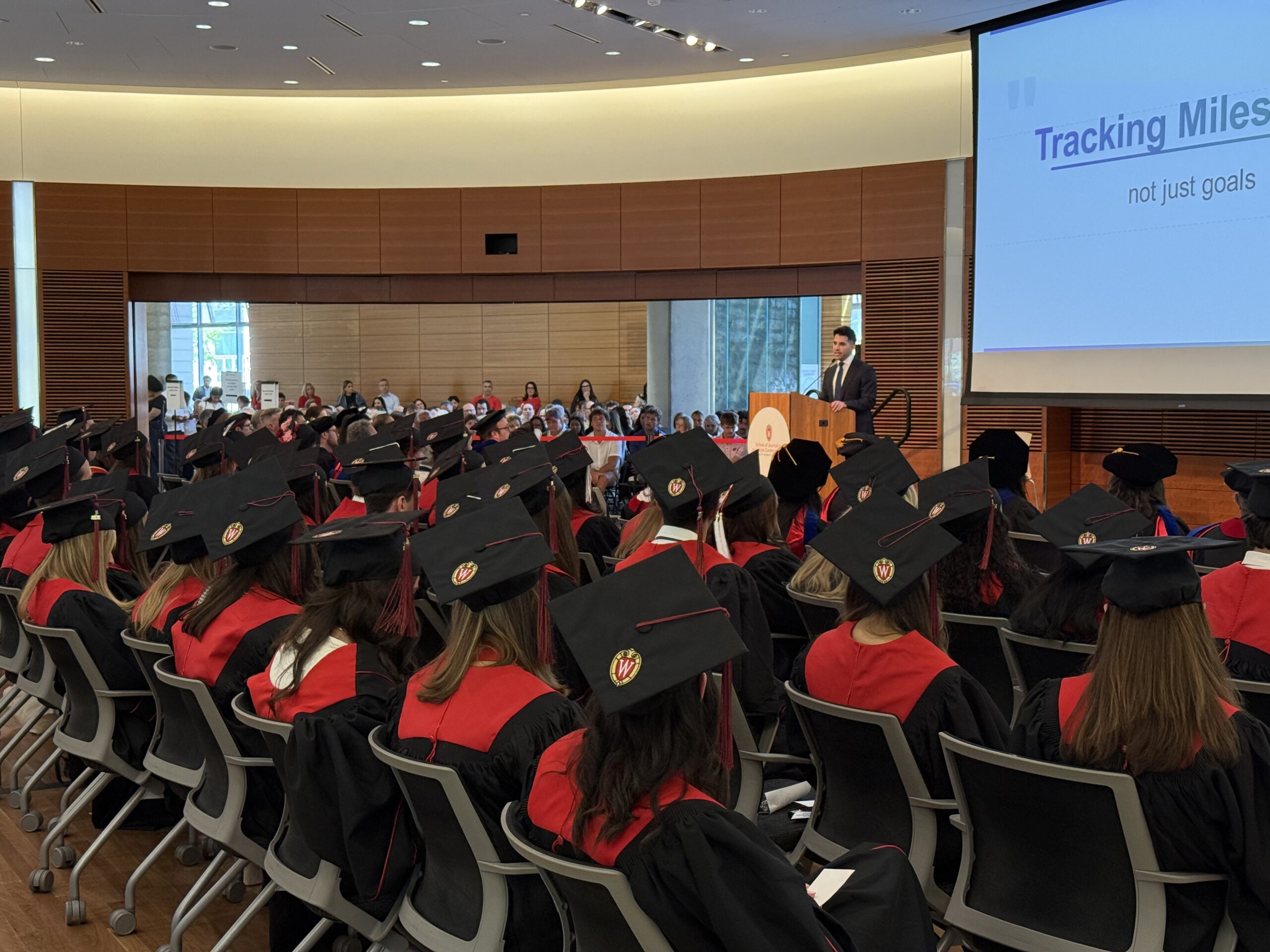 An auditorium filled with graduates watching the keynote speaker at their graduation celebration.