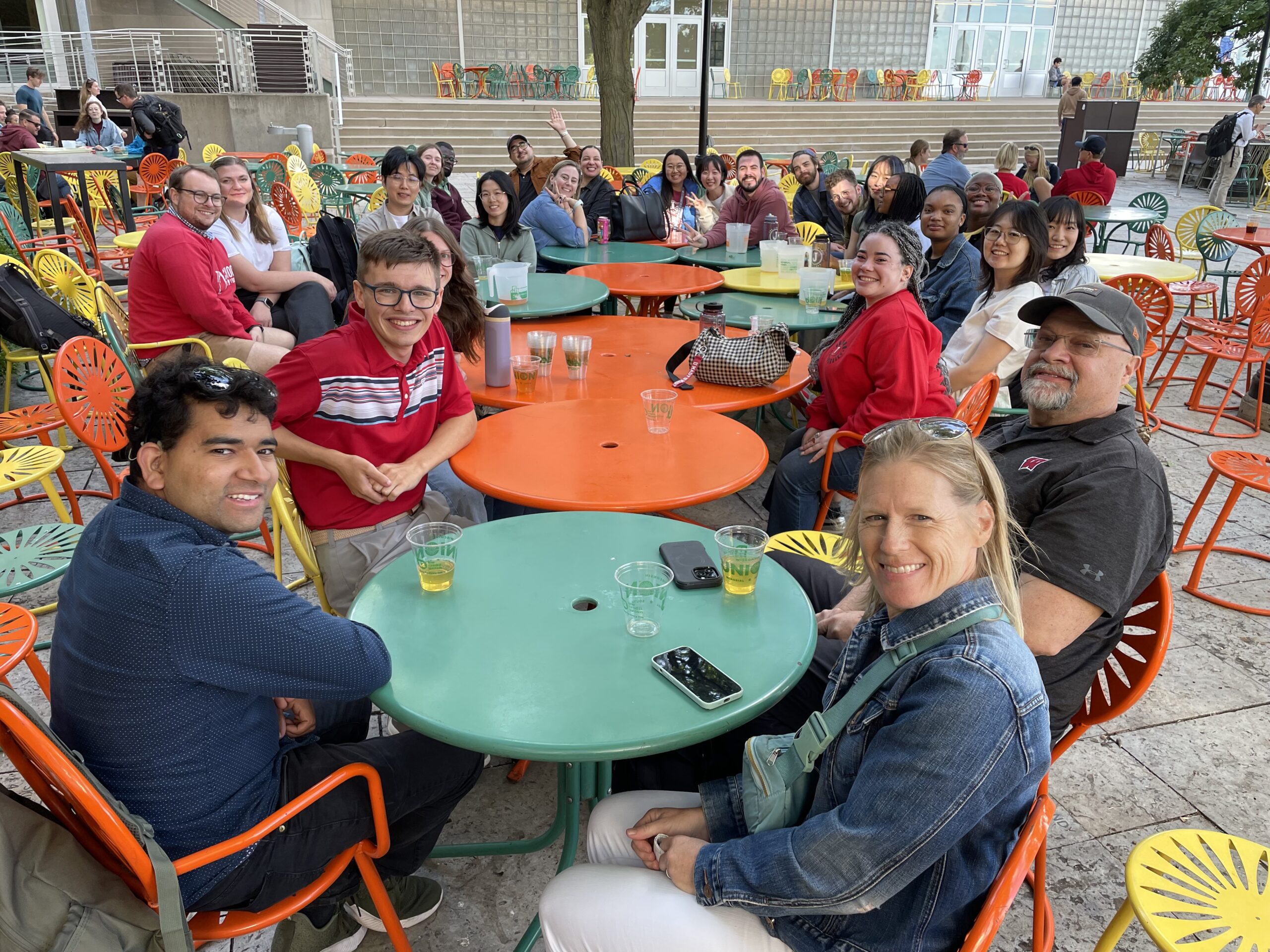 A group of graduate students and faculty members gathered around colorful tables socializing.