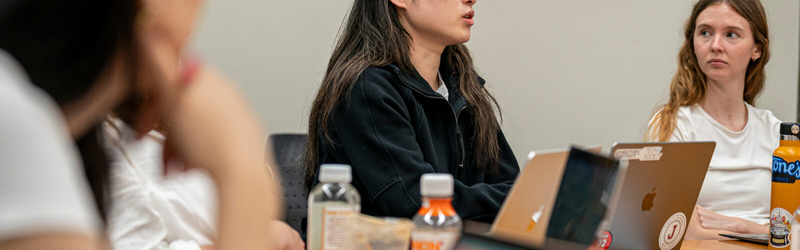 A female grad student talks during a seminar discussion while two female grad students look towards her.