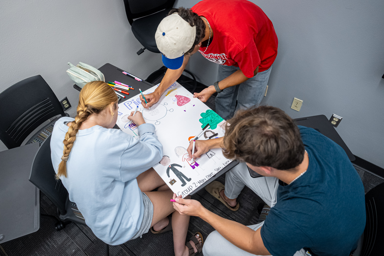 Three students draw on a large poster