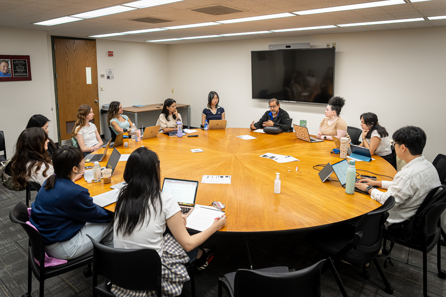 Graduate students sit around a large round wooden table during a research seminar with professor Dhavan Shah.