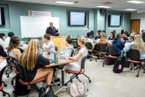 A man with dark hair wearing a black sweatshirt leads a classroom of students