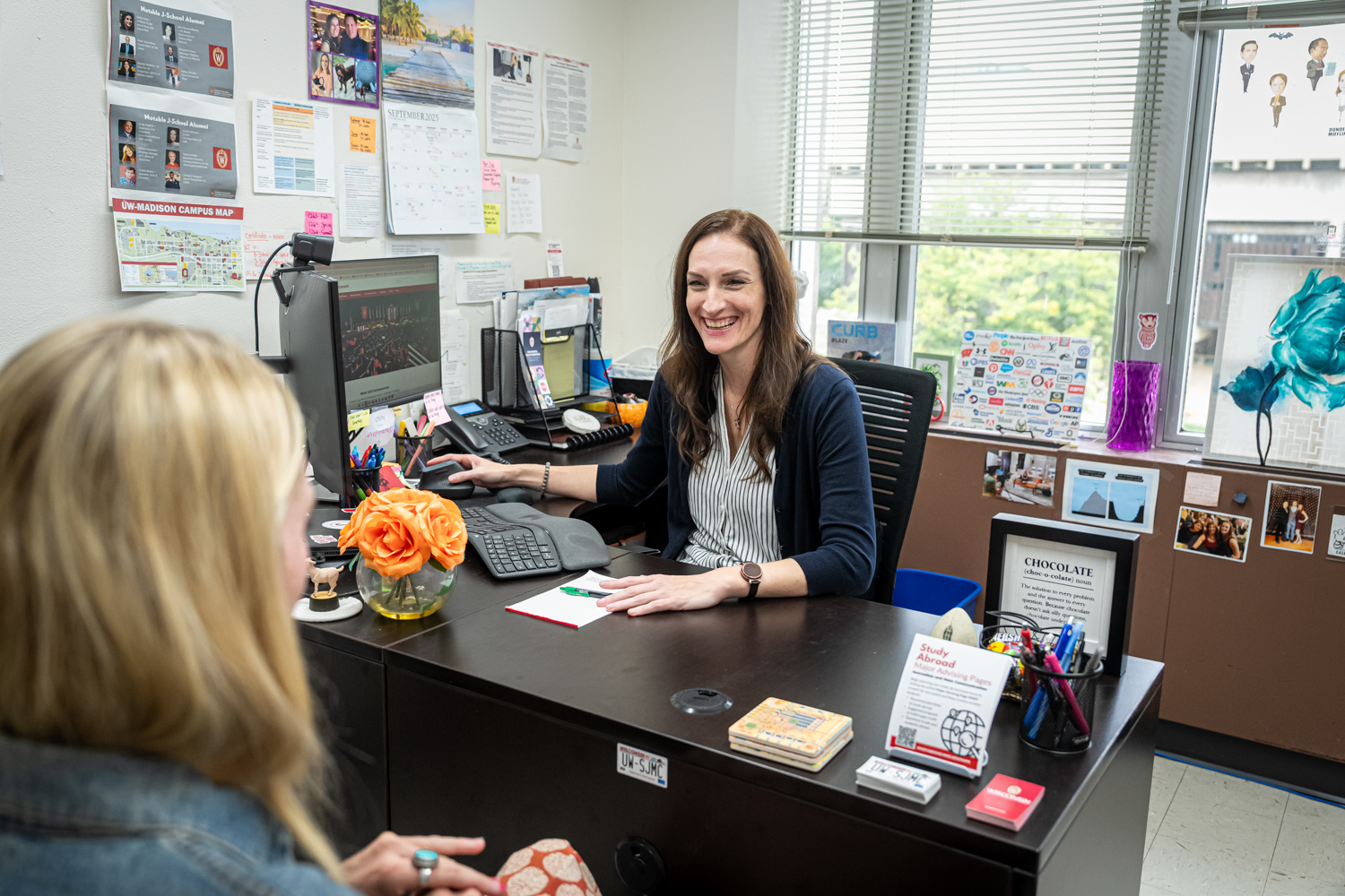 A woman with brown hair in a dark cardigan meets with a female student in her office.