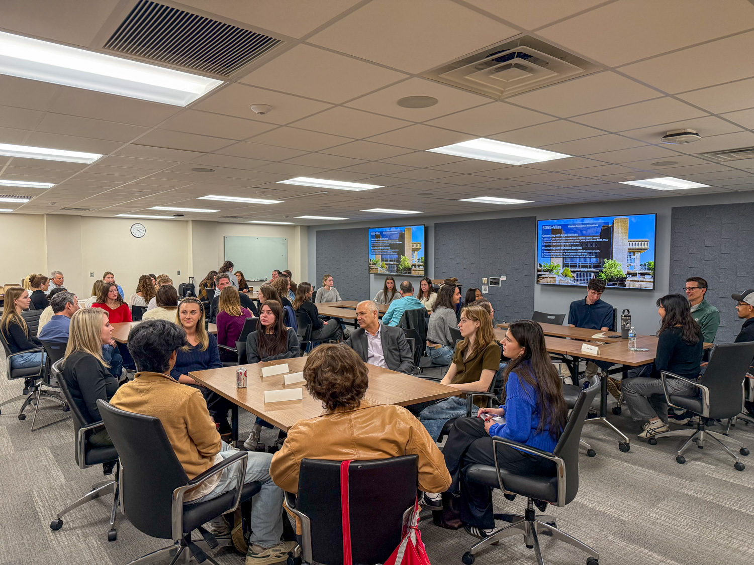 Students meet with alumni in a large classroom in clustered tables.