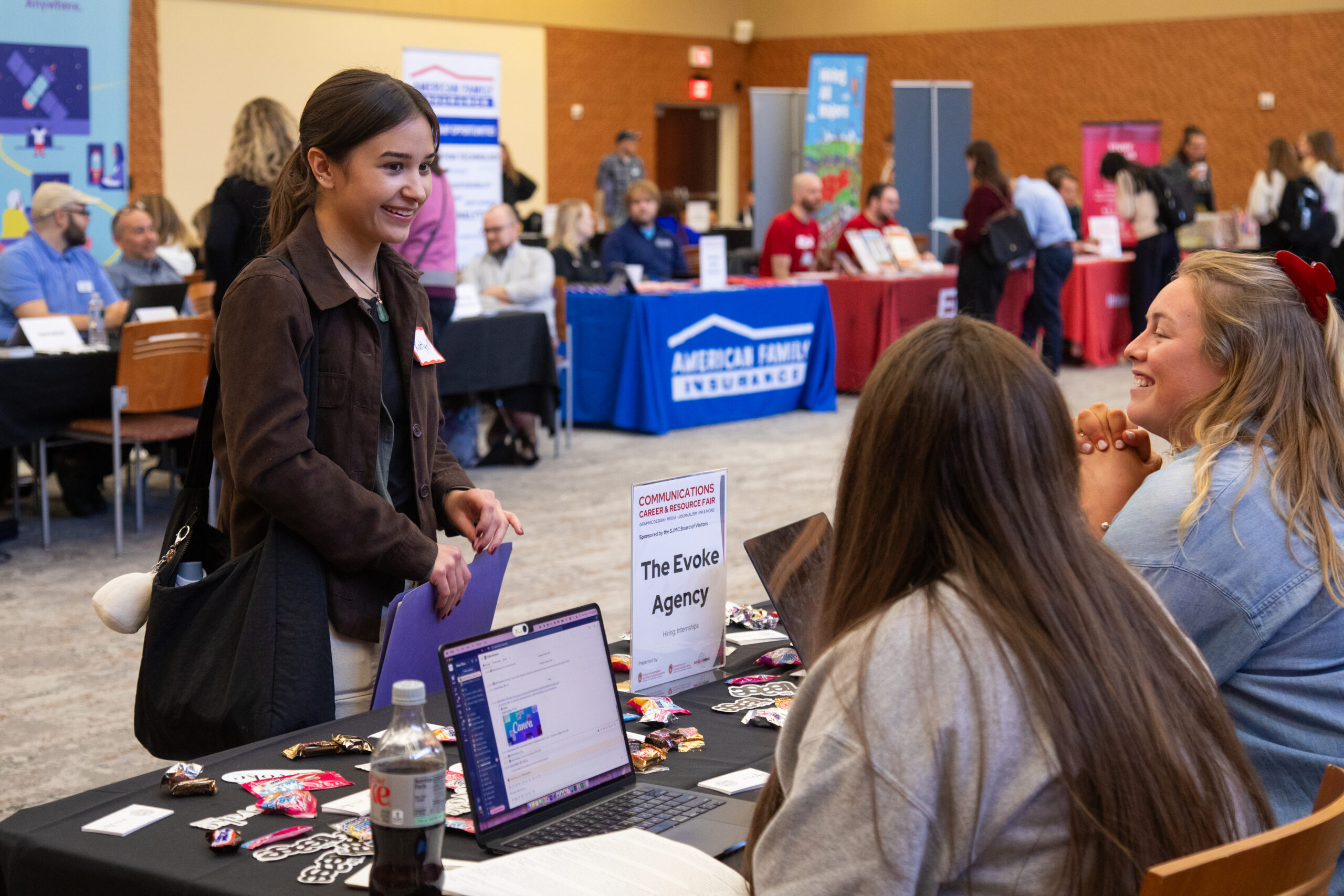 A female student in a dark blazer meets with employers at a career fair.