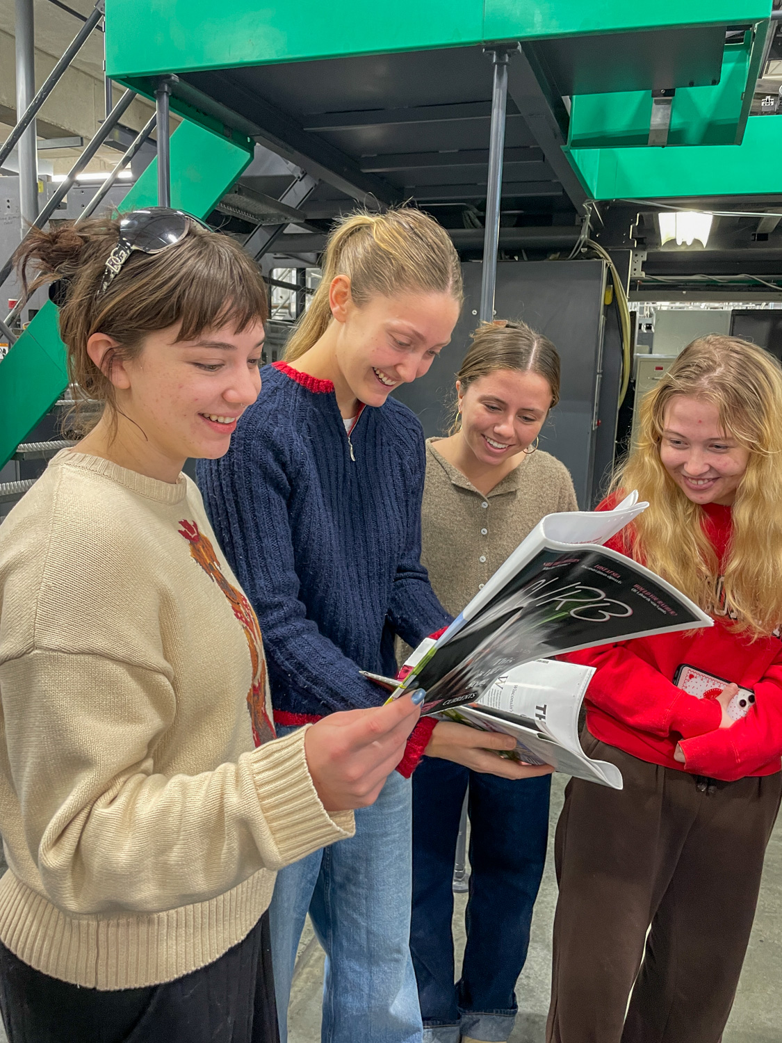 A group of four female students look through a printed magazine
