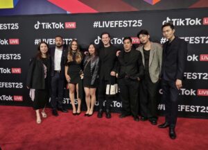 A group of men and women pose together on a red carpet in front of a banner with the TikTok logo and text that reads #LiveFest25