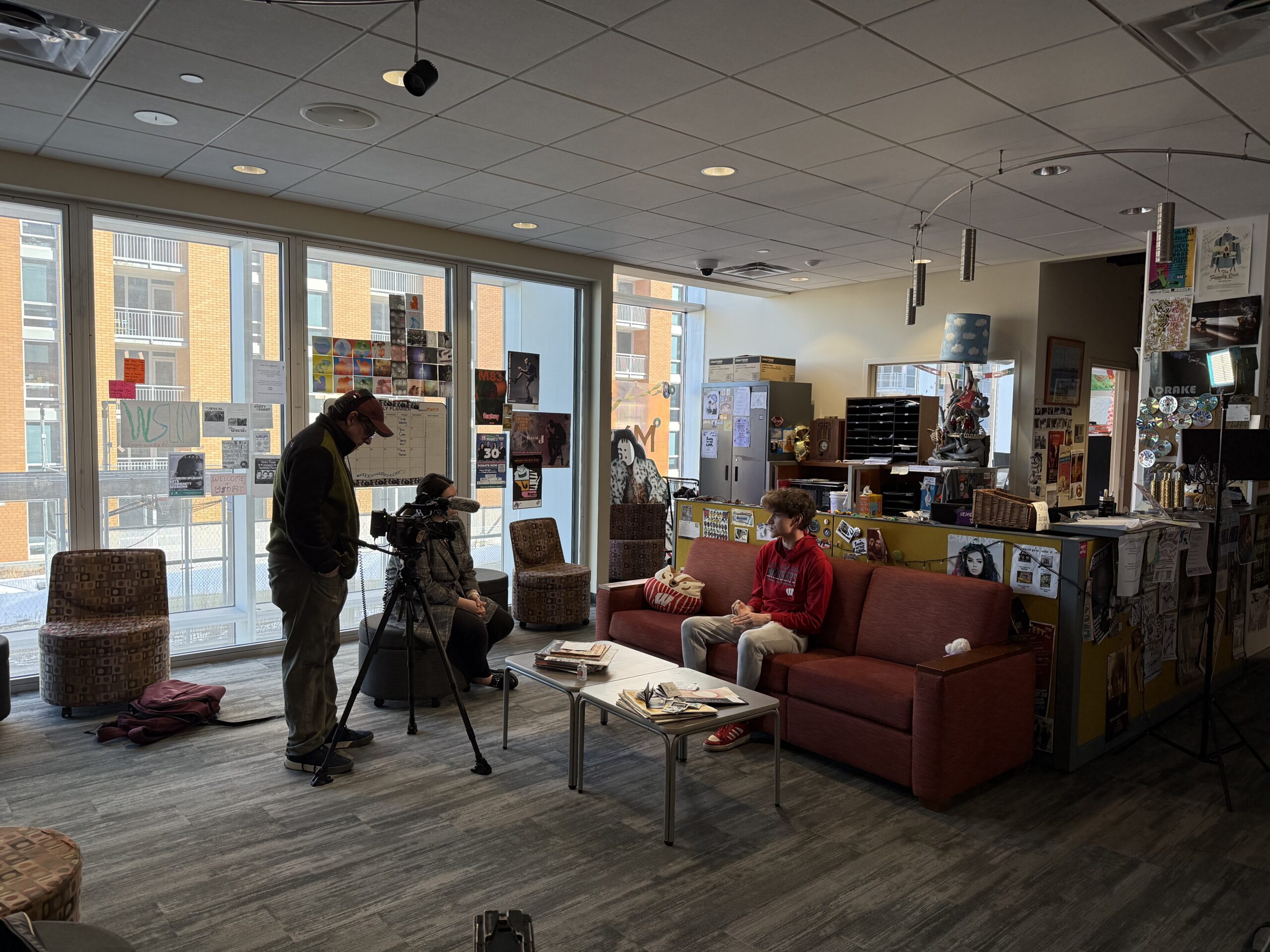 A man in a red sweatshirt is filmed and interviewed by a TV news crew.