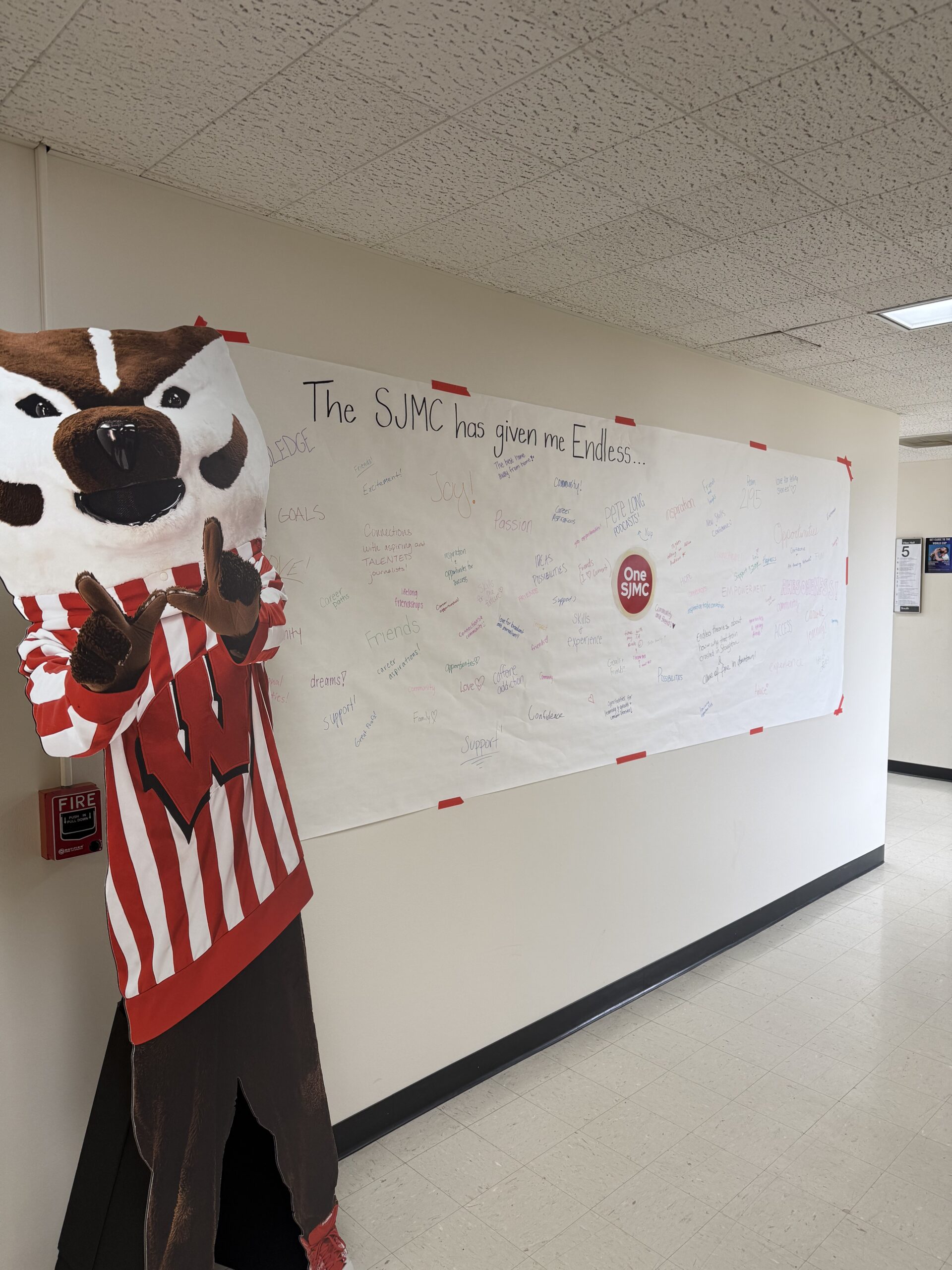 A cardboard cut out of Bucky Badger next to a large wall display that reads "The SJMC has given me endless..." and is filled with students' responses