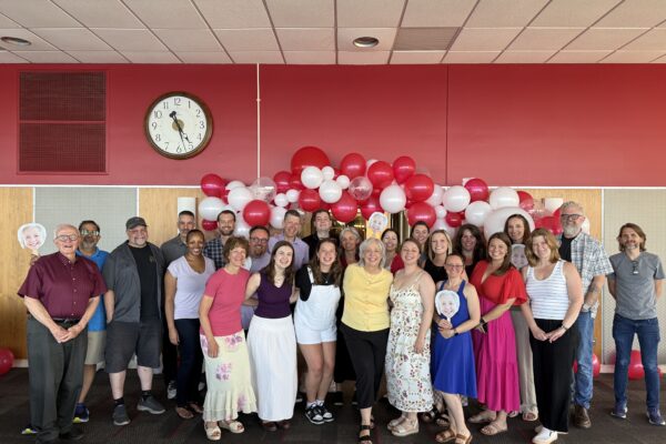 A large group of people pose together under a red and white balloon arch