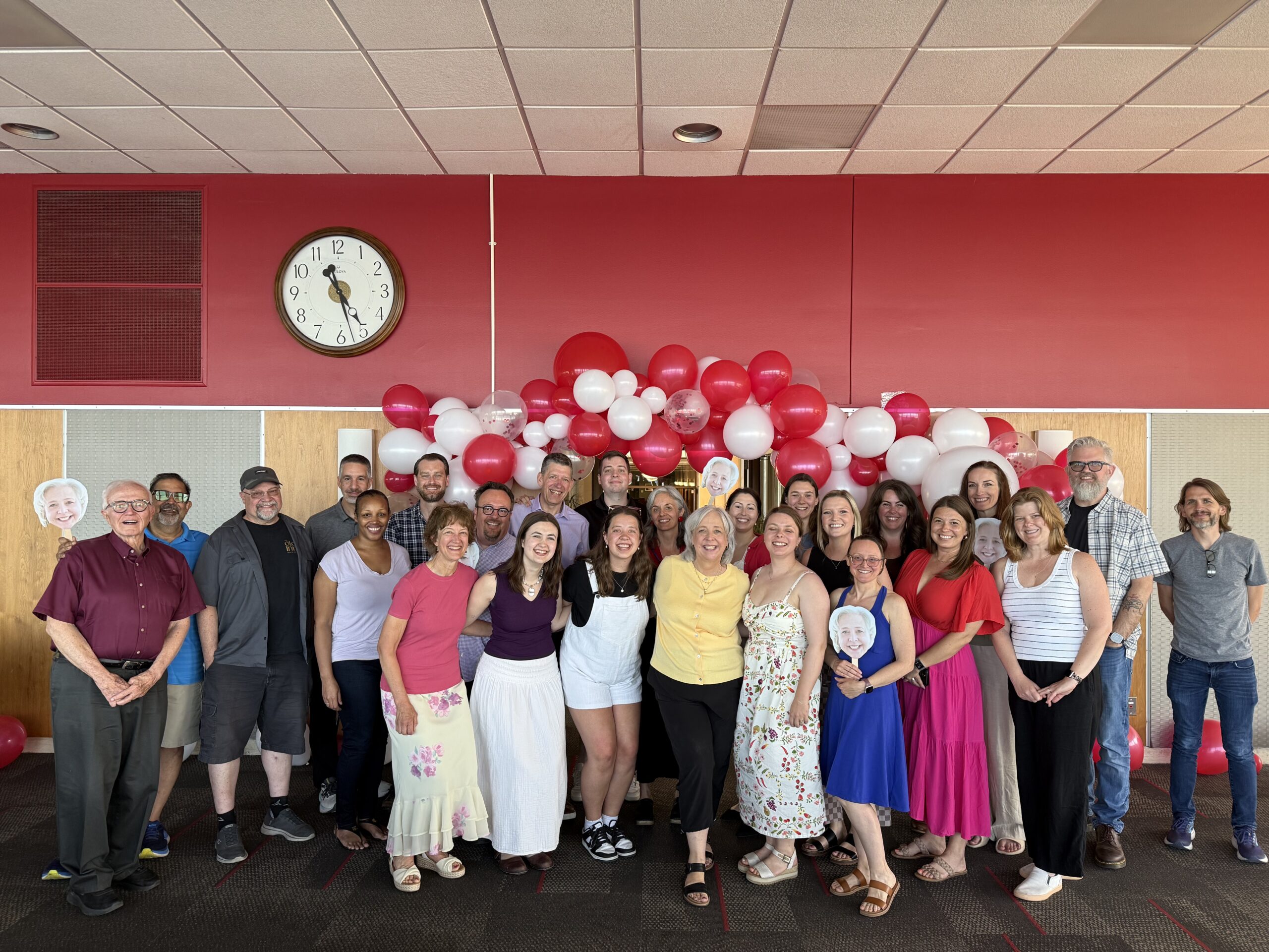 A large group of people pose together under a red and white balloon arch