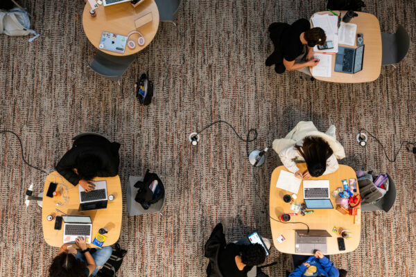 A photo taken from above of students at four tables studying with laptops