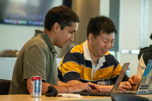 Two men smile while working together on laptops
