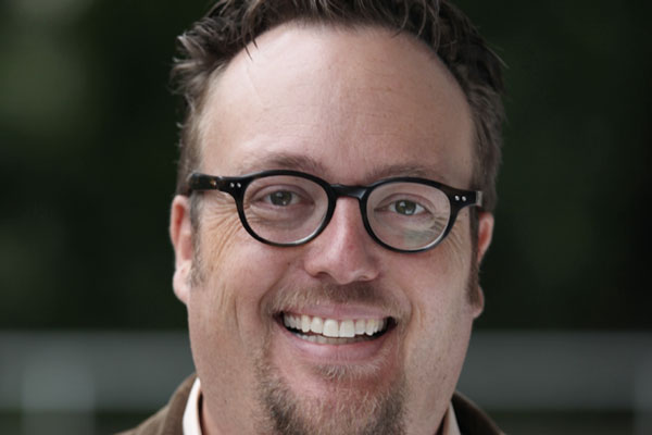 A man with brown hair and glasses smiling.