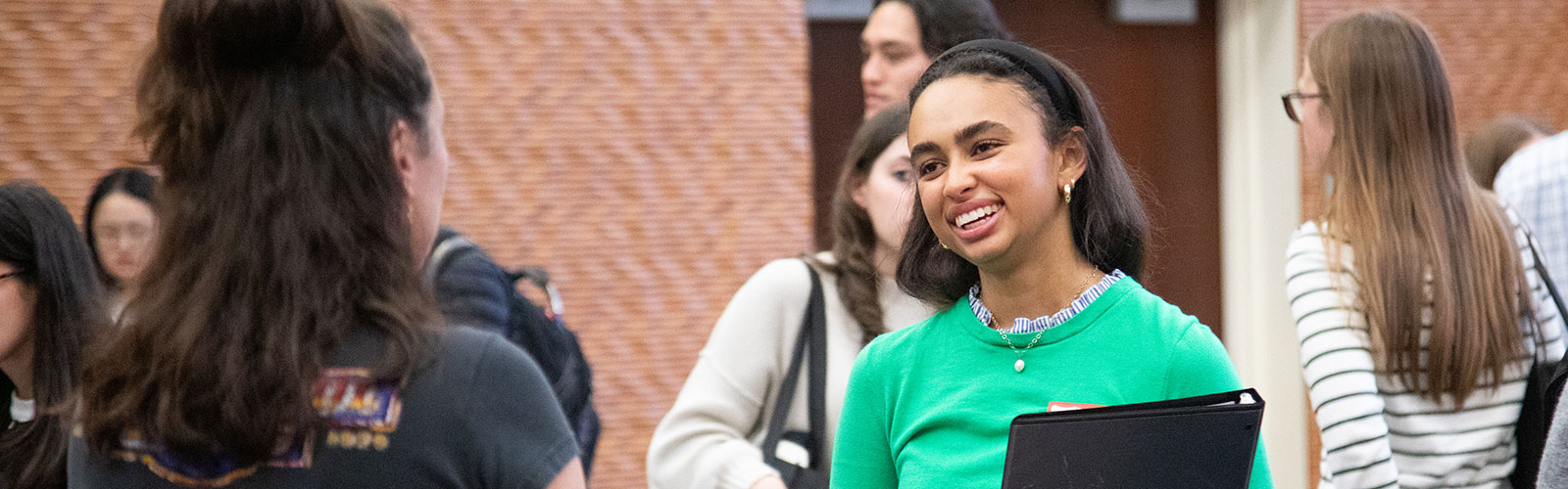 A girl with dark hair and wearing a green shirt smiles while talking to a woman with long brown hair