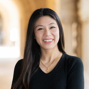 Professional headshot of a smiling woman with long dark hair, wearing a black shirt.